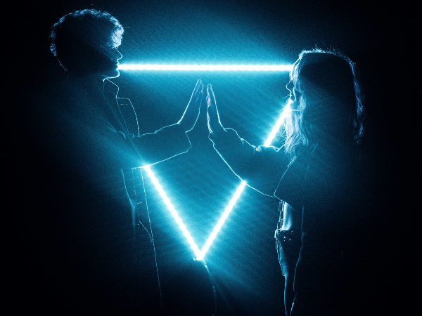 Upside-down glowing triangle behind the silhouette of two humans facing one another, palms about to touch 