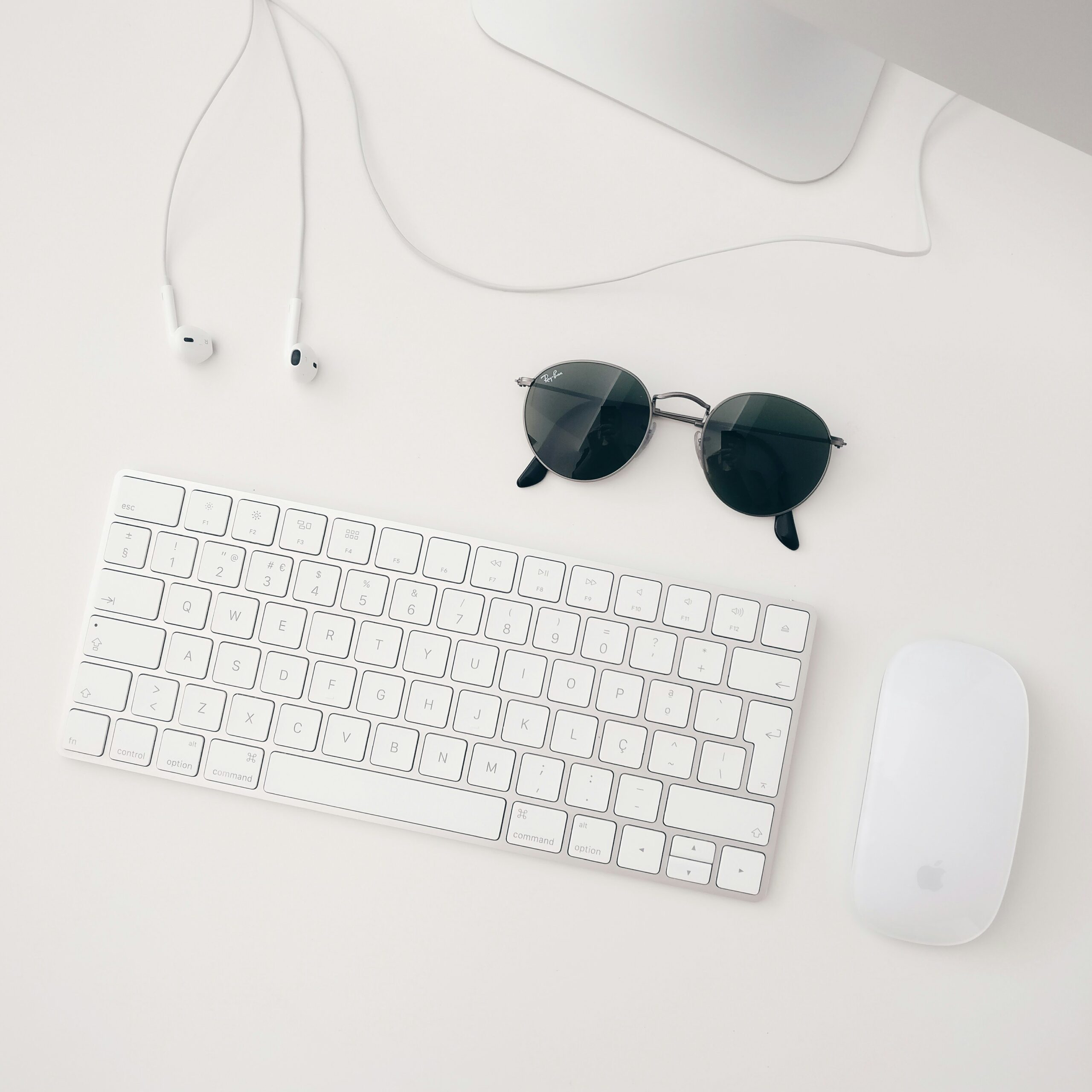 Photo of sunglasses, keyboard, headphones, mouse, depicting a simple office workspace